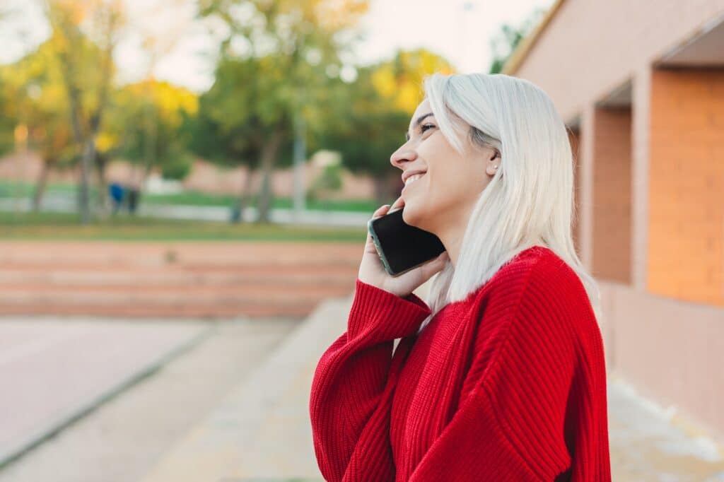 Girl with silver hair sitting and speaking with her phone. Dressed in a red sweater.